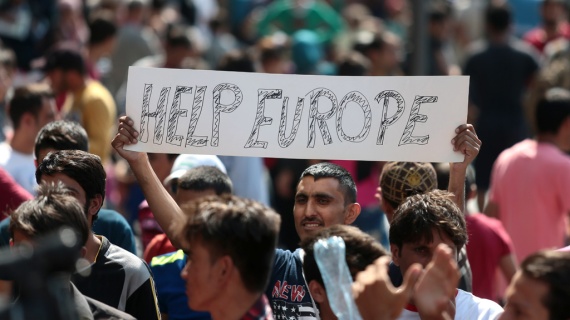 A man hold a placard reading "Help Europe" as Syrian and Afgan refugees attend a protest rally to demand to travel to Germany on September 2, 2015 outside the Keleti (East) railway station in Budapest. Hungarian authorities face mounting anger from thousands of migrants who are unable to board trains to western European countries after the main Budapest station was closed.  AFP PHOTO / FERENC ISZA        (Photo credit should read FERENC ISZA/AFP/Getty Images)